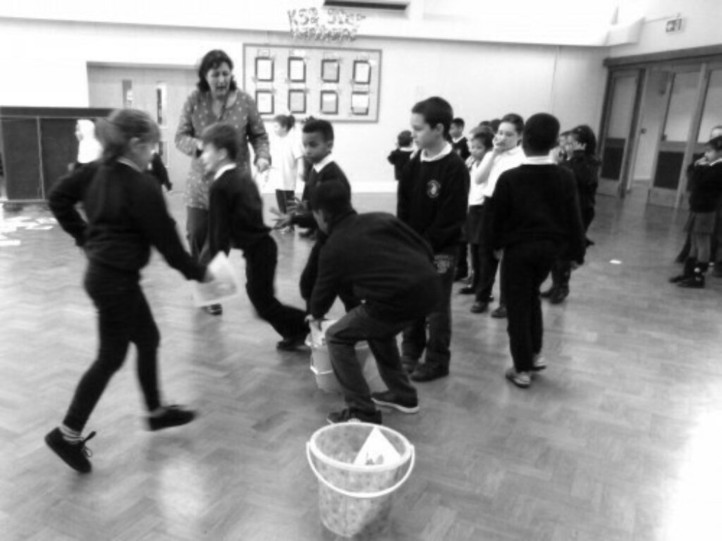 Black and white photograph of children engaging in activities run by the project in a school hall.